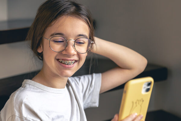 A young girl with glasses and metal braces smiling