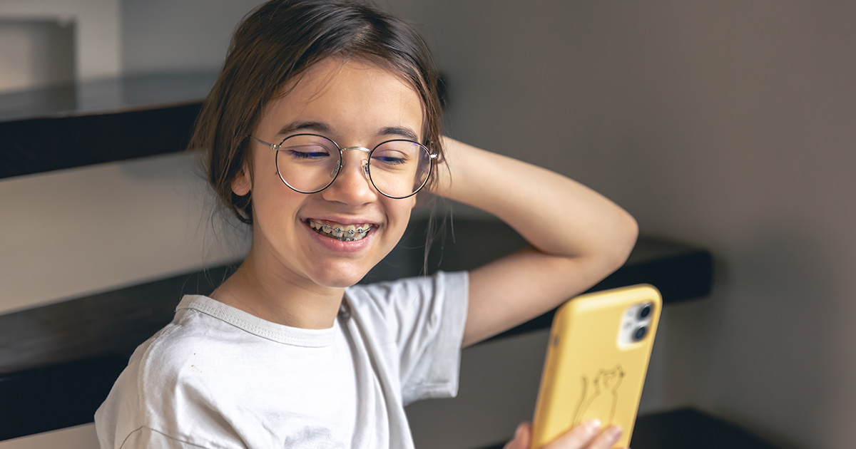 A young girl with glasses and metal braces smiling